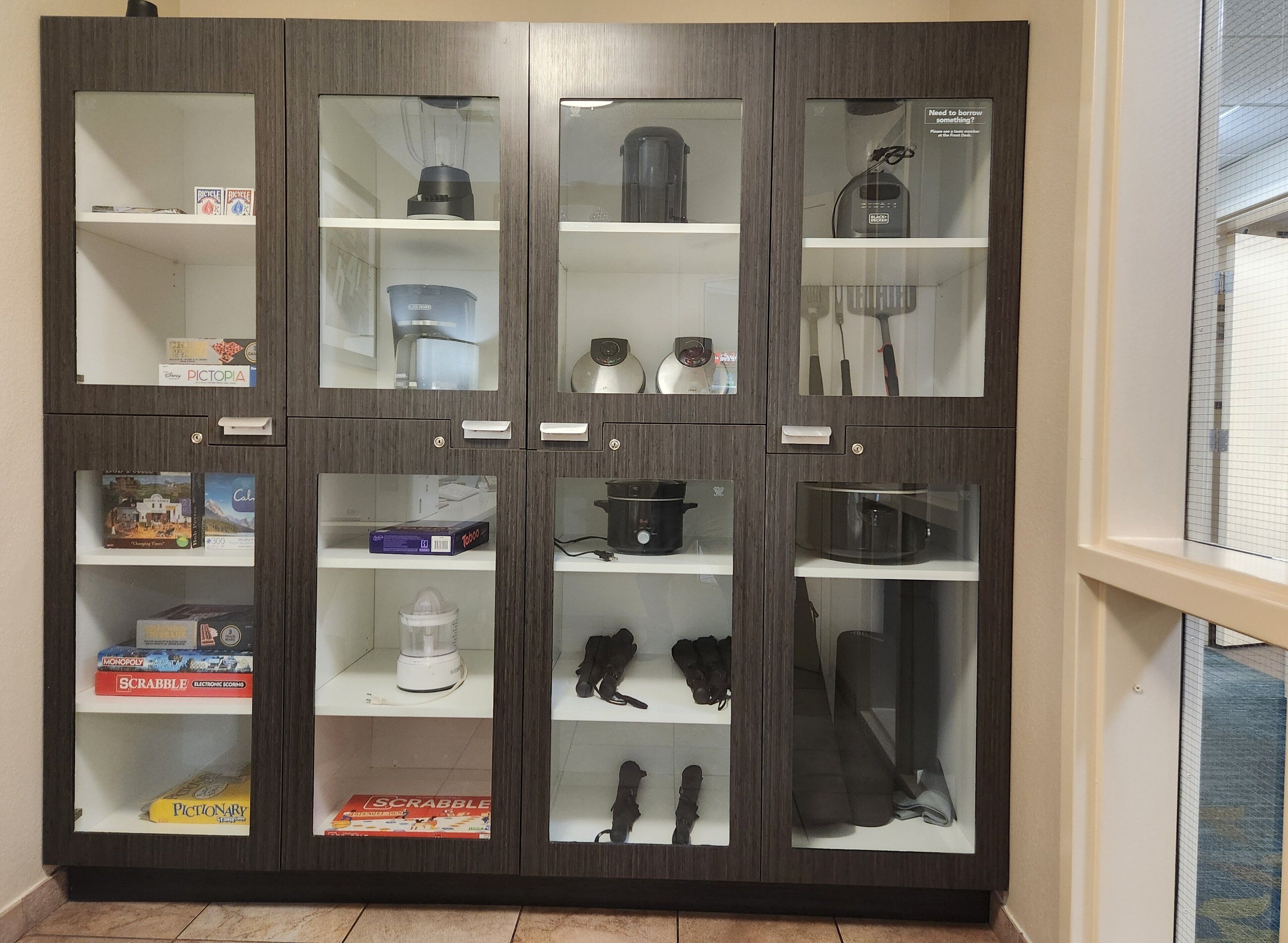 A cabinet with multiple shelves containing various items such as board games, kitchen appliances, and storage containers.