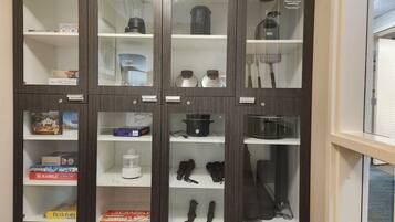 A cabinet with multiple shelves containing various items such as board games, kitchen appliances, and storage containers.