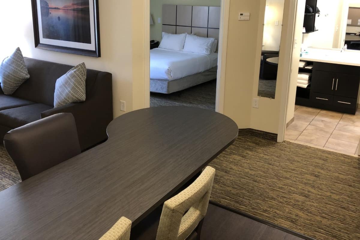 Une chambre d’hôtel moderne avec une table à manger en bois foncé, un canapé et un lit avec une literie blanche.
