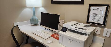 Een hotel werkplek met een bureau, computer, printer, stoel, lamp en een lijst in een lijstwerk.