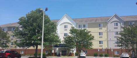 A multi-story hotel with a central entrance, parking lot, and surrounding greenery.