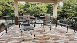 An outdoor patio with a brick floor, metal chairs, a table, and two barbecue grills. - Candlewood Suites Greenville NC by IHG (Greenville)