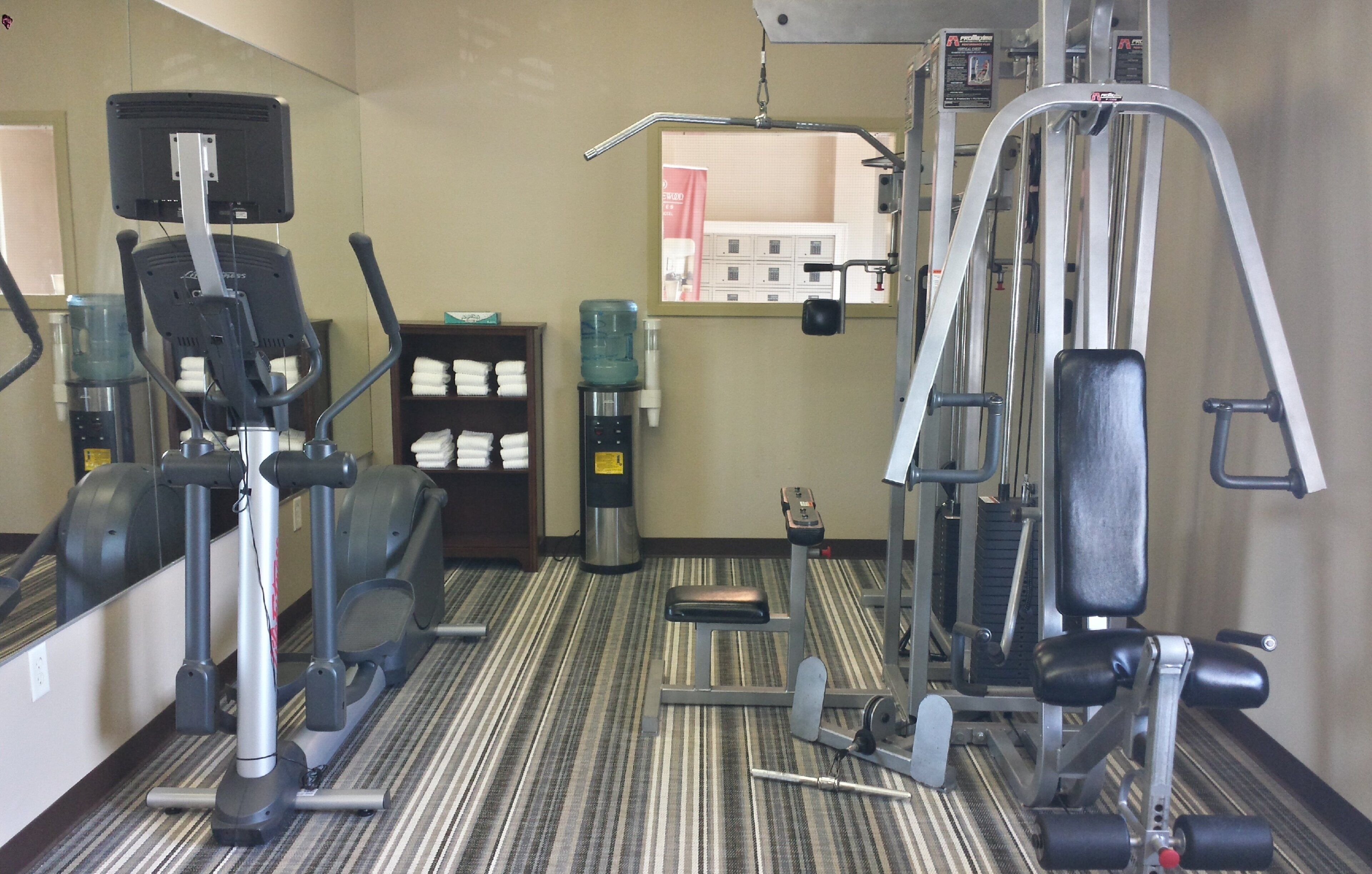 A fitness center with exercise equipment, a water dispenser, and towels on shelves.