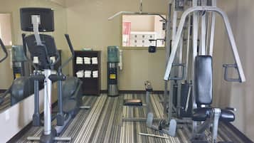 A fitness center with exercise equipment, a water dispenser, and towels on shelves.
