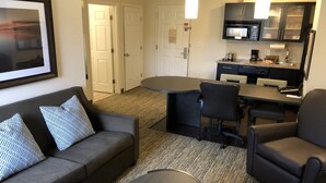A hotel room with a sofa, a round table, a dining table with chairs, a kitchen area with a microwave, and a framed picture on the wall. - Candlewood Suites Greenville NC by IHG (Greenville)
