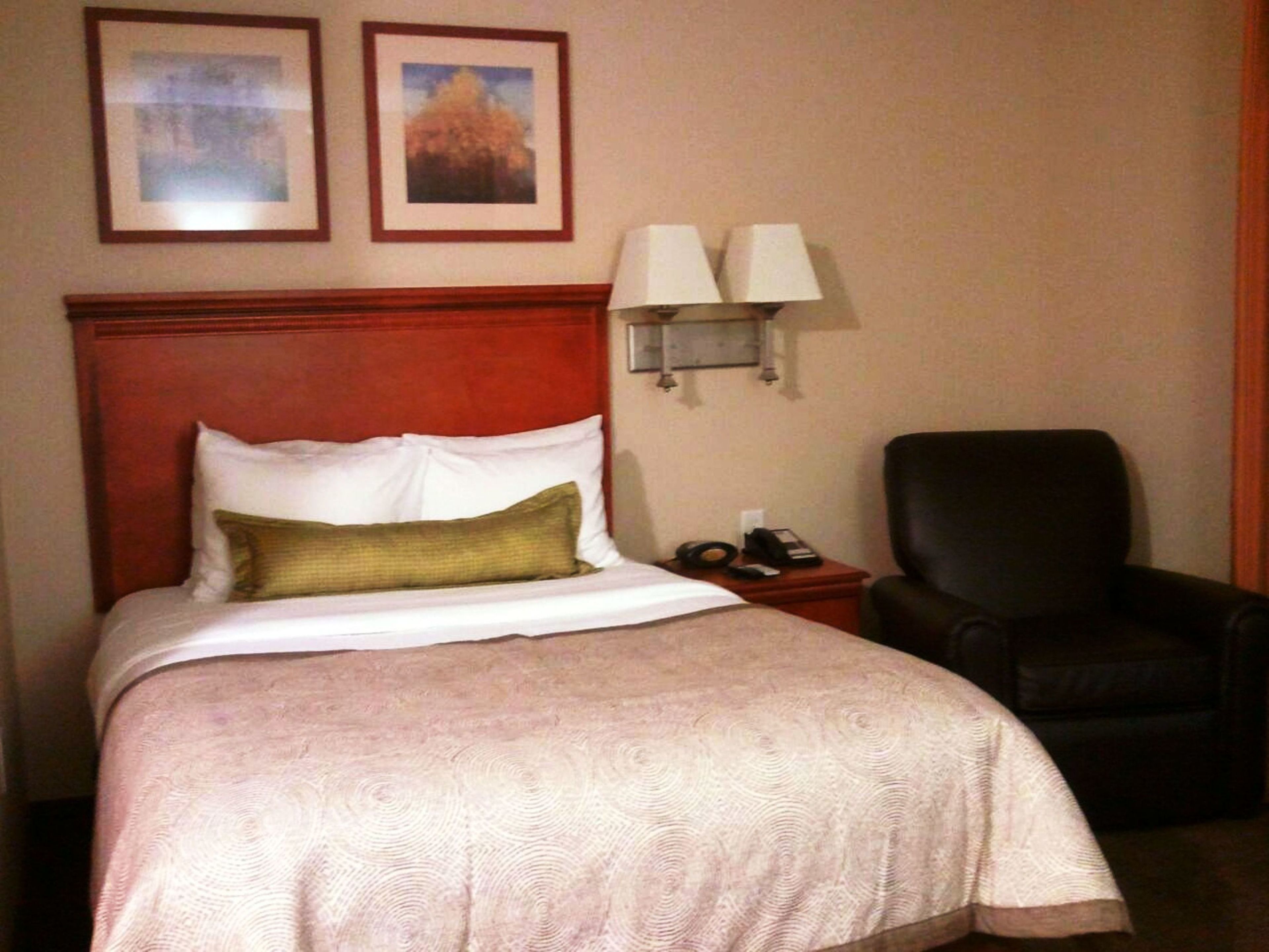 A hotel room with a bed, a chair, a nightstand with a phone, and two wall-mounted lamps.