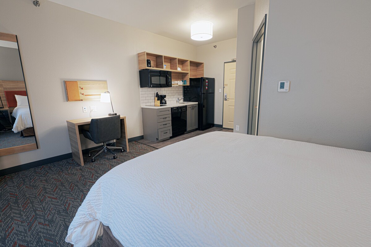 Une chambre d’hôtel avec un grand lit, un bureau avec une chaise, un four à micro-ondes, un réfrigérateur et une petite kitchenette.