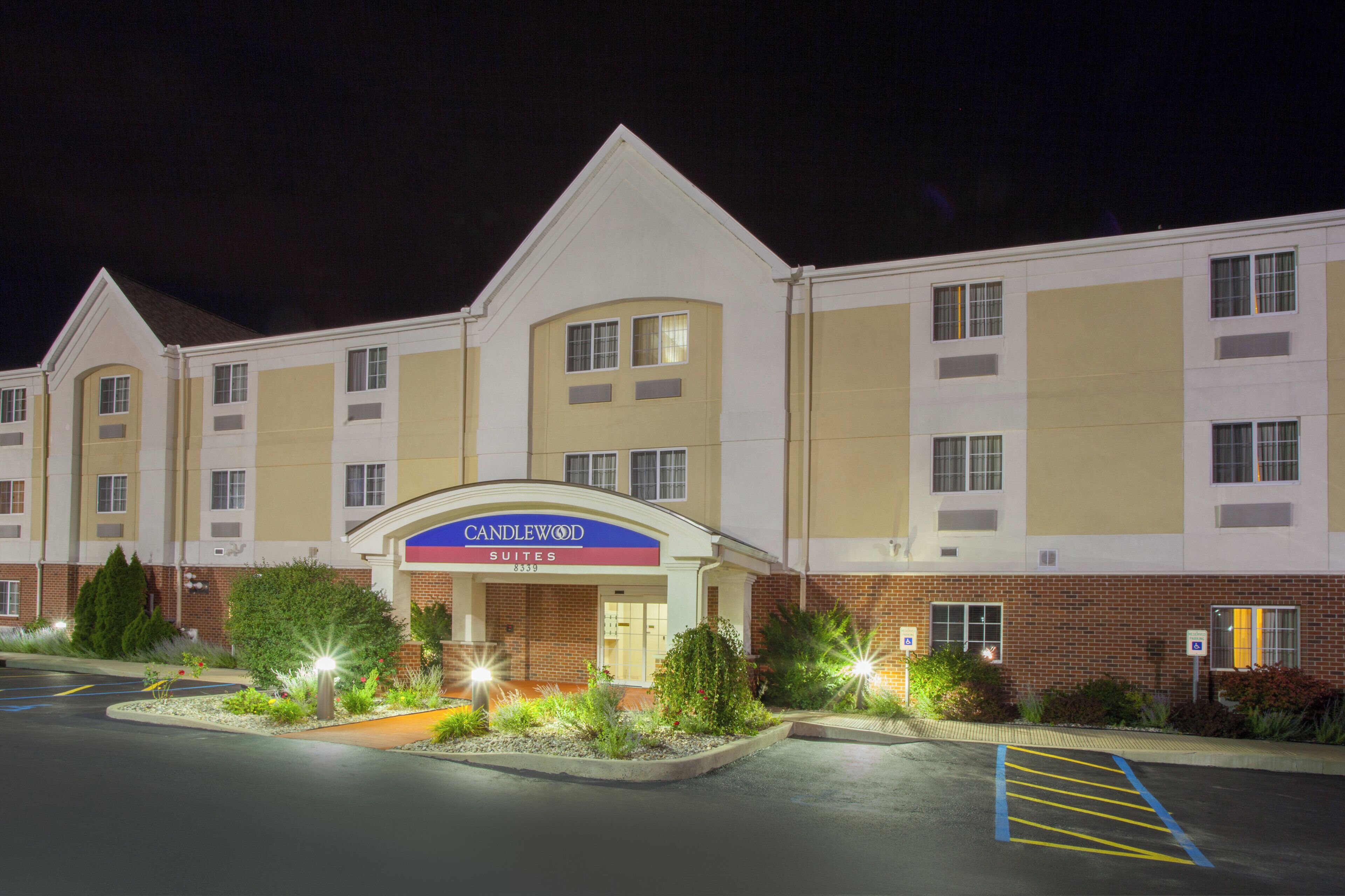 Um hotel com um letreiro chamativo de 'Candlewood Suites', fachada de tijolos e um estacionamento com vagas demarcadas.