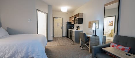 Habitación de hotel con cama, escritorio, silla y kitchenette.