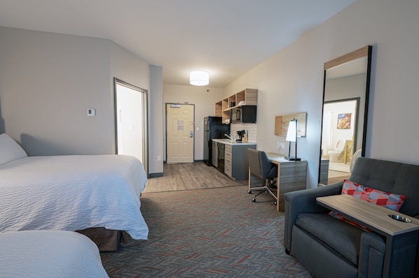 A hotel room with two beds, a desk with a chair, a kitchenette, and a large mirror. - Candlewood Suites Merrillville by IHG (Merrillville)