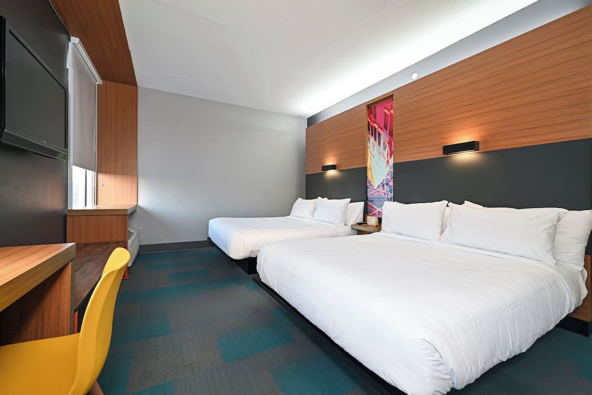 A hotel room with two beds, a desk, and a chair.