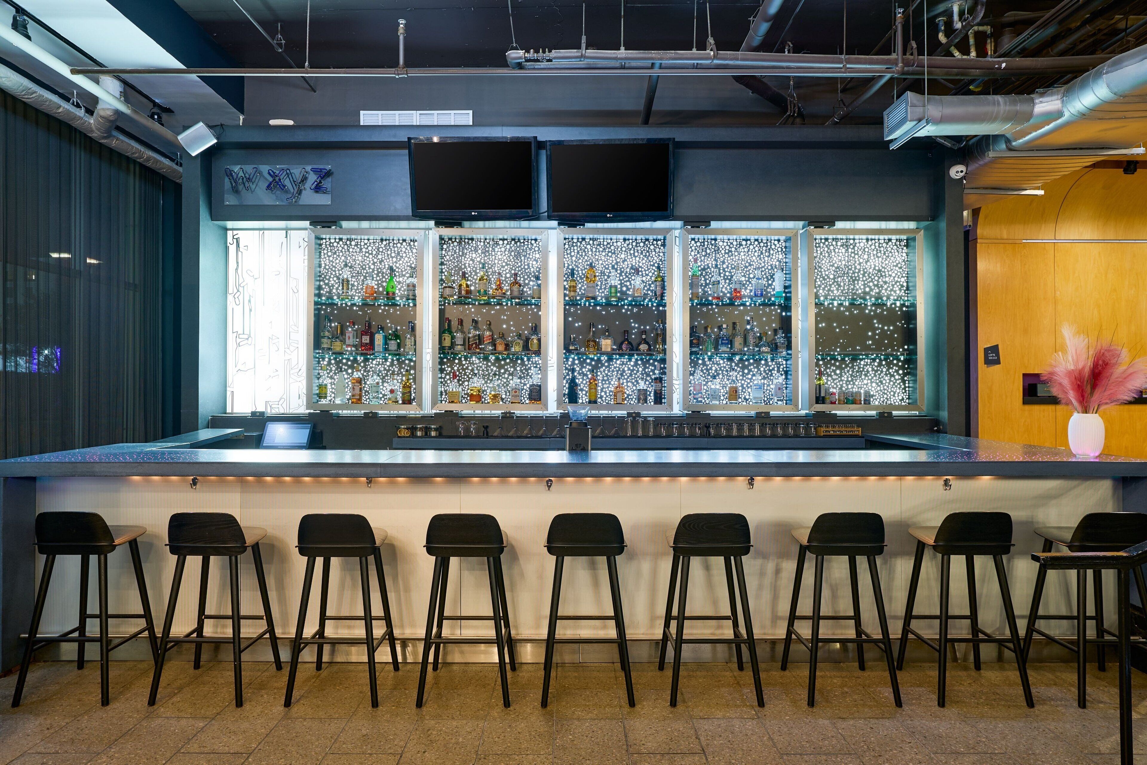 A bar area with a counter, multiple stools, and shelves of bottles.