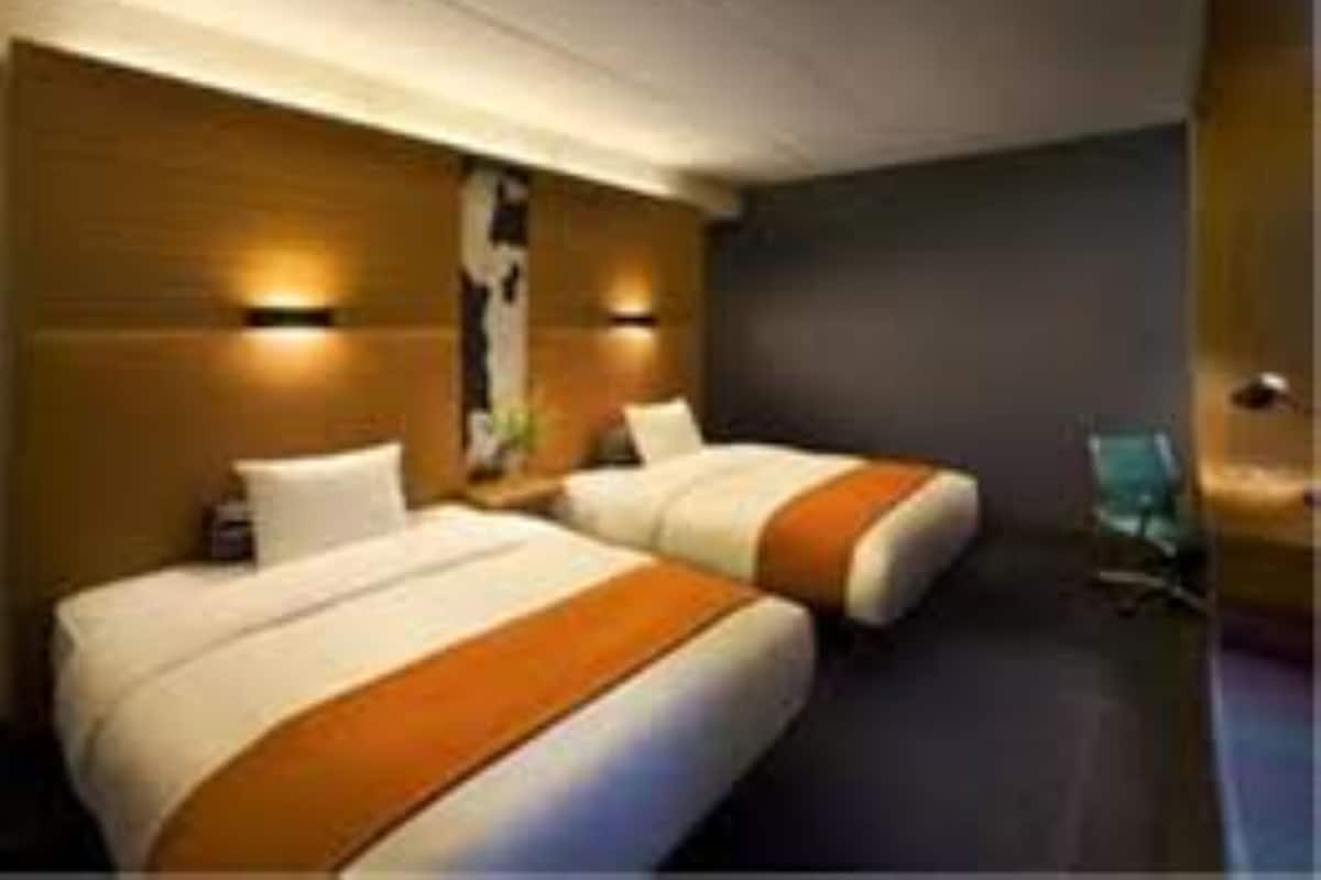 A hotel room with two beds, wooden headboards, and wall-mounted lighting.