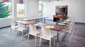 A conference room with a long table, white chairs, a flat-screen TV, and a large window.