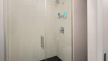 A glass-enclosed shower with a tiled floor and a handrail.