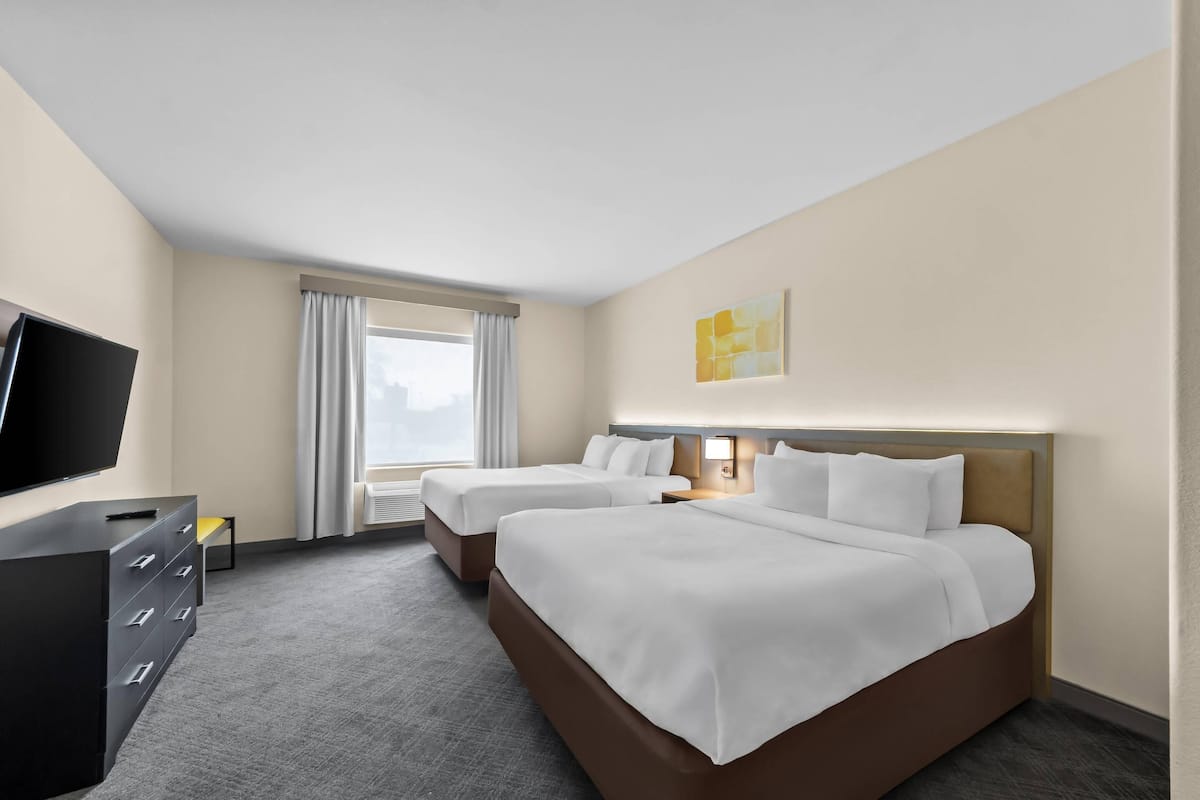 Ein Hotelzimmer mit zwei Betten, einem Fernseher, einer Kommode und einem Fenster mit Vorhängen.