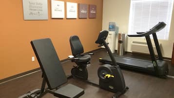 Une salle de sport équipée d’un vélo d’appartement, d’un tapis de course et d’un banc de musculation.