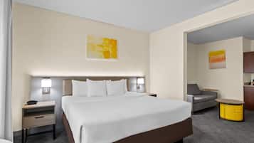 Habitación de hotel con una cama grande, mesitas de noche, un sofá, una pequeña mesa y obras de arte en las paredes.