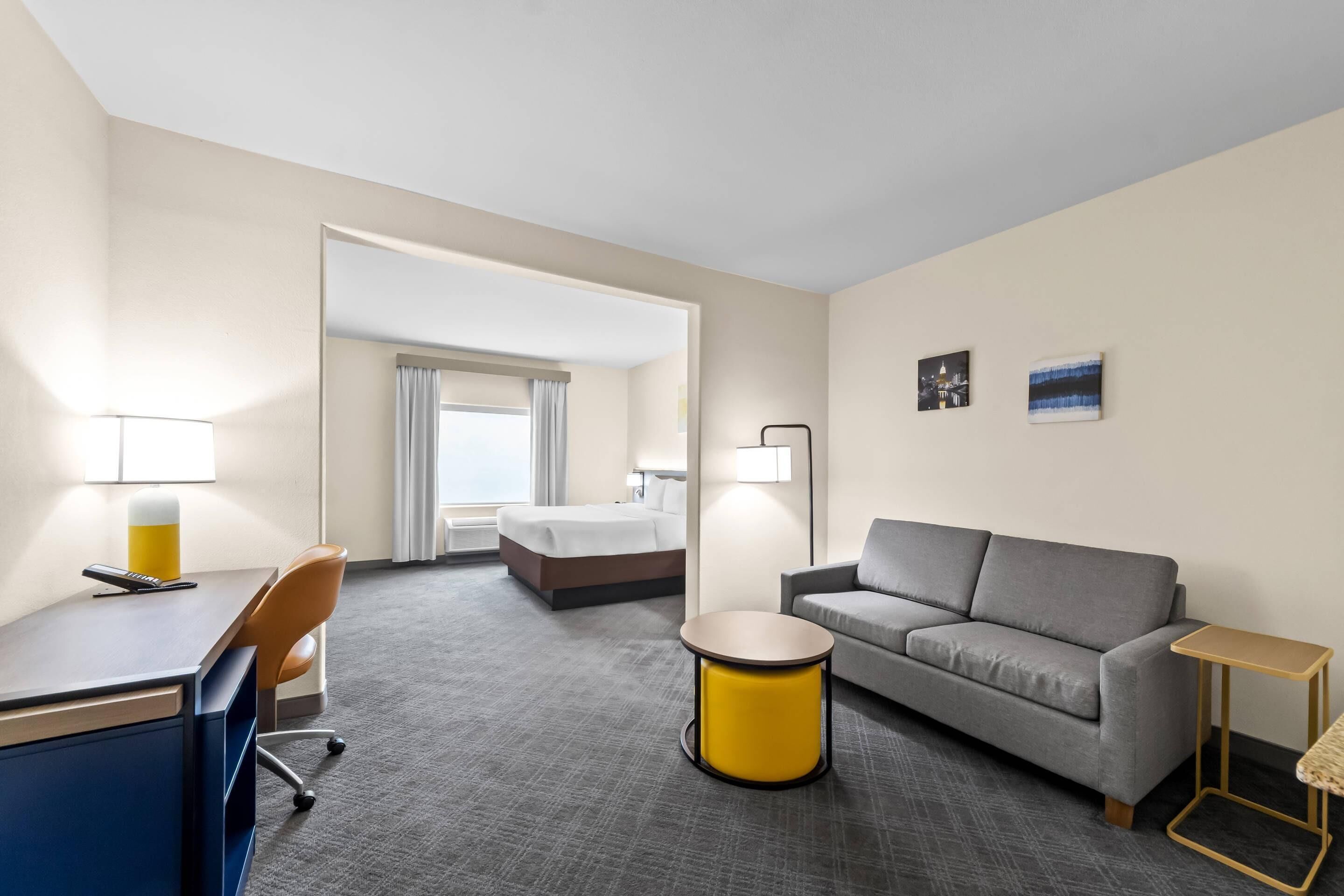 Habitación de hotel con cama, sofá, escritorio, silla y una pequeña mesa redonda.