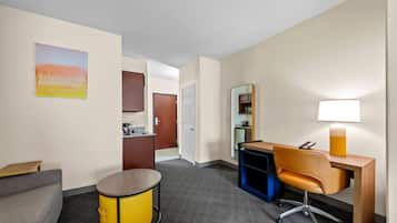 A hotel room with a sofa, a desk, a lamp, a small table, a cabinet, and a door leading to a bathroom.