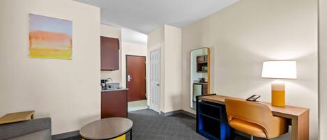 A hotel room with a sofa, a desk, a lamp, a small table, a cabinet, and a door leading to a bathroom.