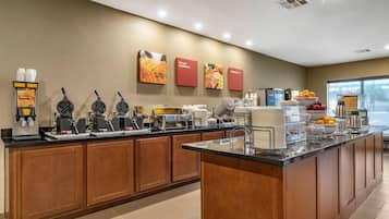 Zona de desayuno de hotel con máquinas para hacer gofres, cafeteras y un bol de fruta.