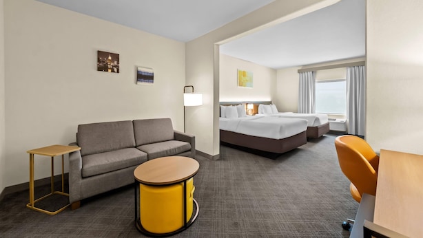 A hotel room with a sofa, a round table, a bed, a lamp, and a window with curtains. - Comfort Suites San Antonio North - Stone Oak (San Antonio)