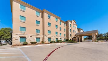 Un hotel de varios pisos con fachada de piedra, un acceso cubierto y cielo despejado.