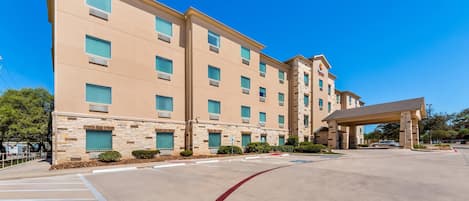 A multi-story hotel with a stone facade, a covered entrance, and a clear sky.