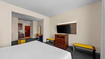 A hotel room with a bed, a TV, a wooden dresser, a bench, and a small table.