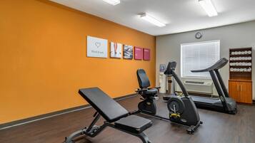 Un gimnasio con una banca, elíptica, bicicleta estática, un reloj y una ventana con persianas.