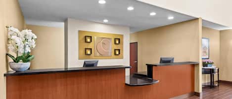 A reception area with wooden reception desks, a wall-mounted clock, and a potted plant.