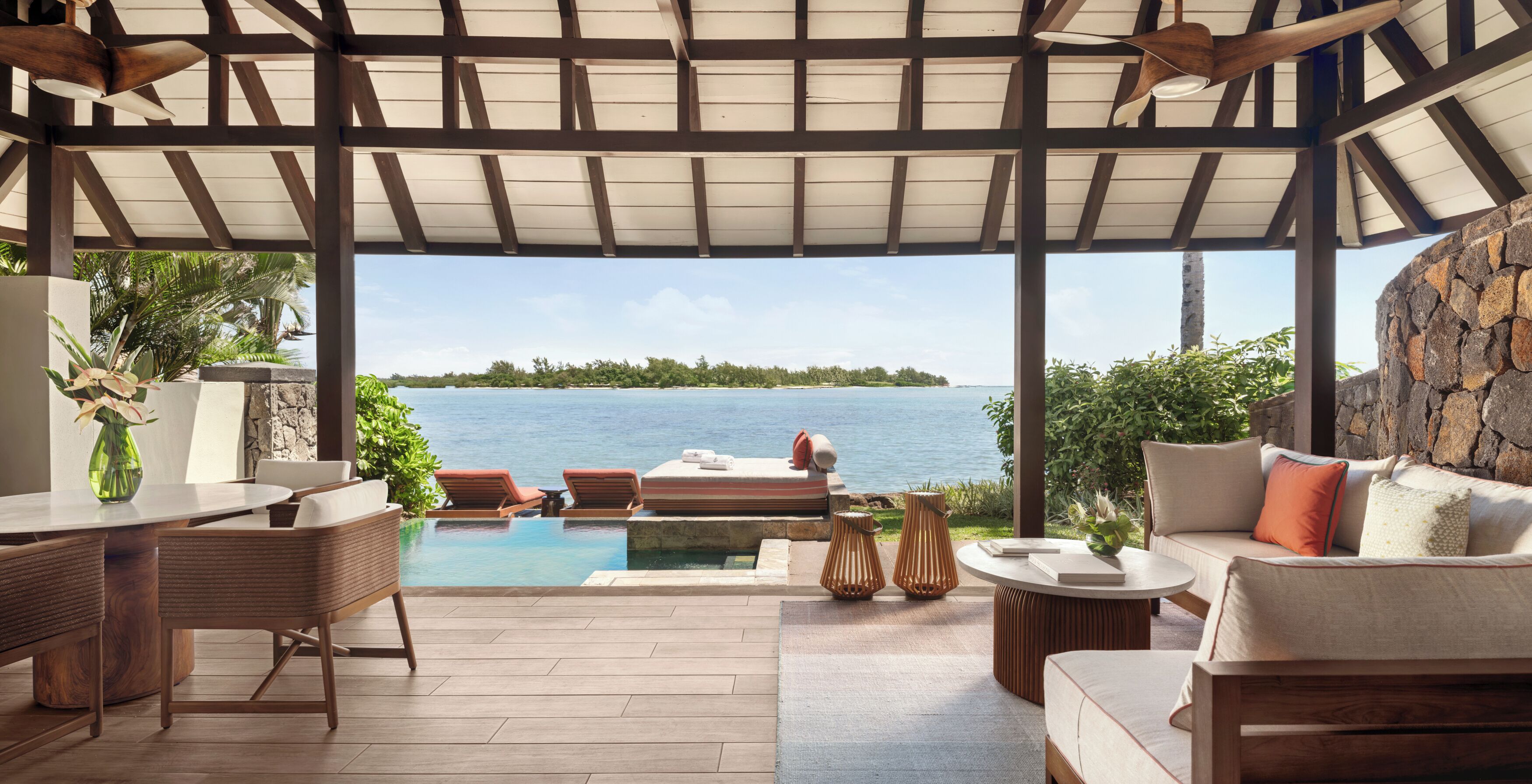 A covered outdoor area with a pool, lounge chairs, and a view of the sea.