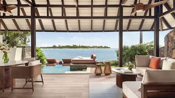 A covered outdoor area with a pool, lounge chairs, and a view of the sea.