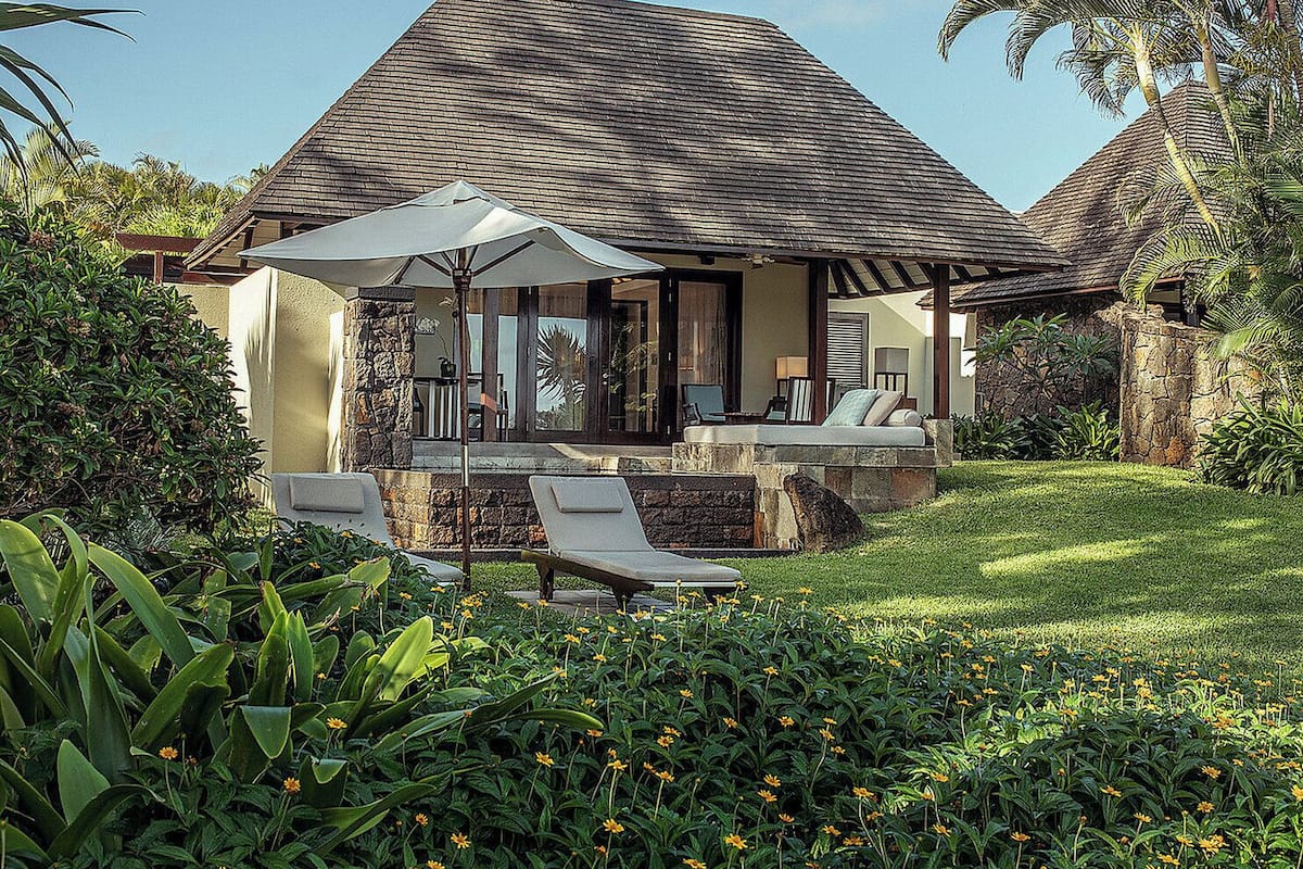 A house with a sloped roof, a patio with lounge chairs, and a garden with yellow flowers.