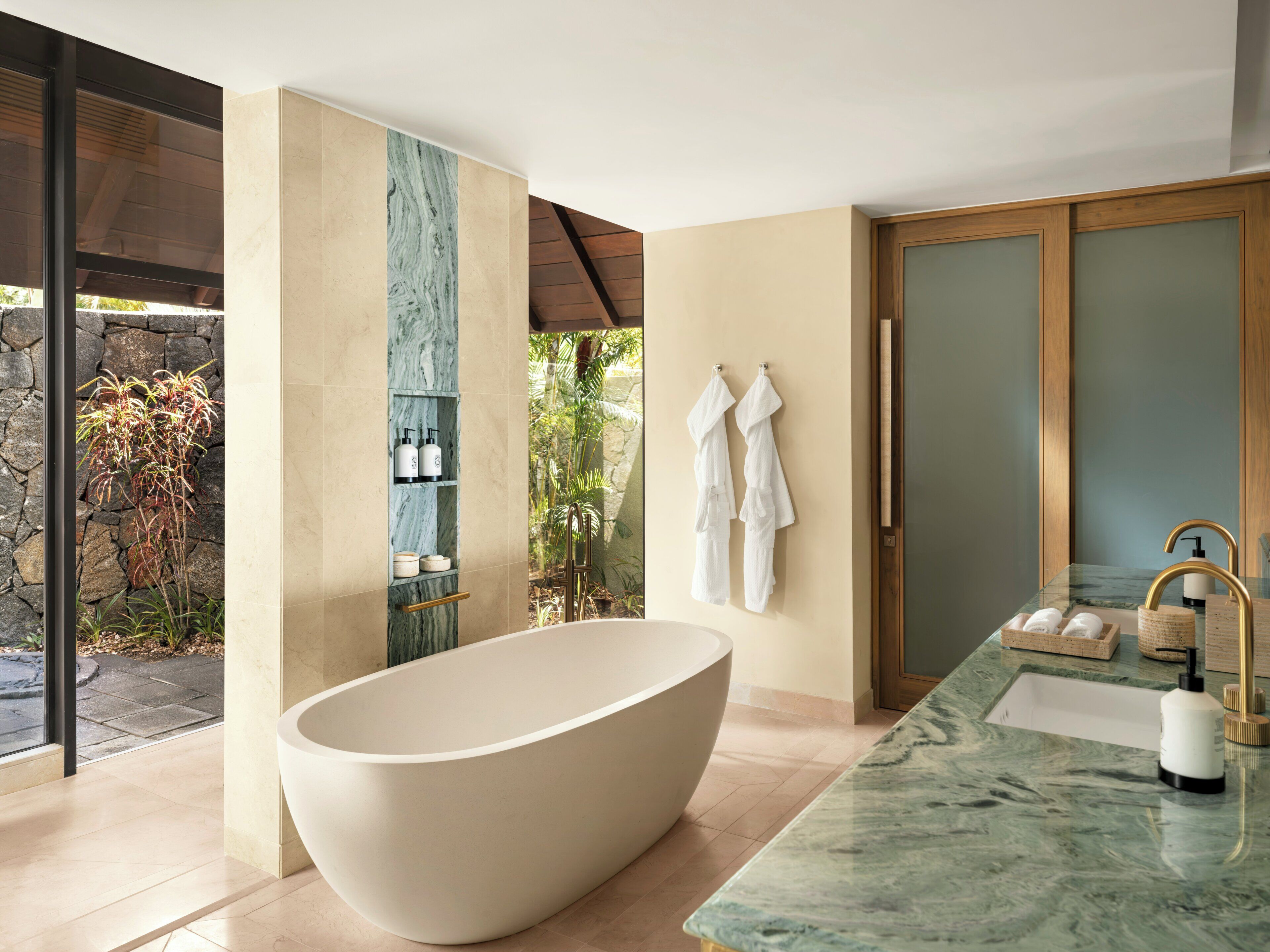 A modern bathroom with a freestanding bathtub, marble countertop, and a view of greenery outside.