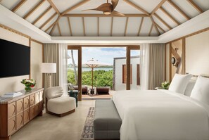 A bedroom with a large bed, a TV, a desk, and a view of the outdoors.