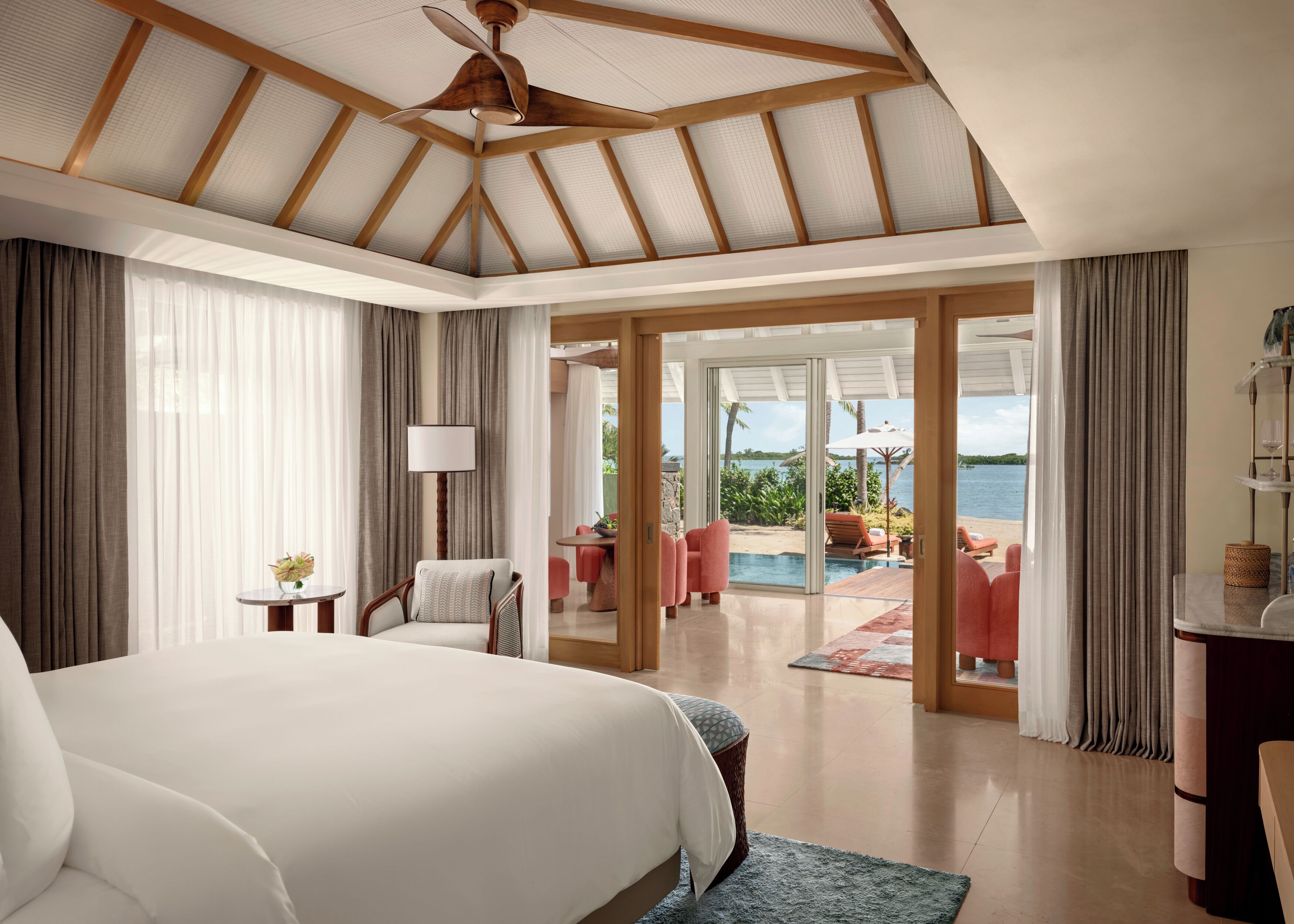 Ein Schlafzimmer mit einem großen Bett, einem Deckenventilator, Blick auf einen Außenpool und eine Lounge-Area sowie einer Glastür zum Pool.