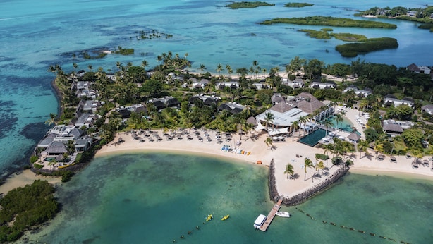 Vista aerea di un resort con diverse sistemazioni tipo bungalow, una zona piscina centrale e una spiaggia con ombrelloni e lettini.