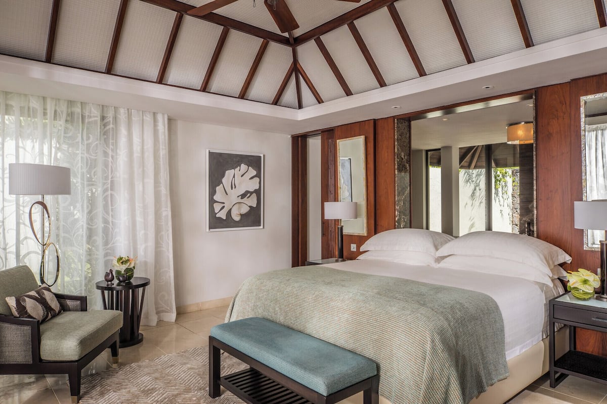 A bedroom with a large bed, a chair, a small table, and a mirror.