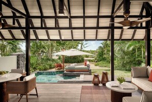 A covered outdoor area with a pool, seating, and a view of a garden.