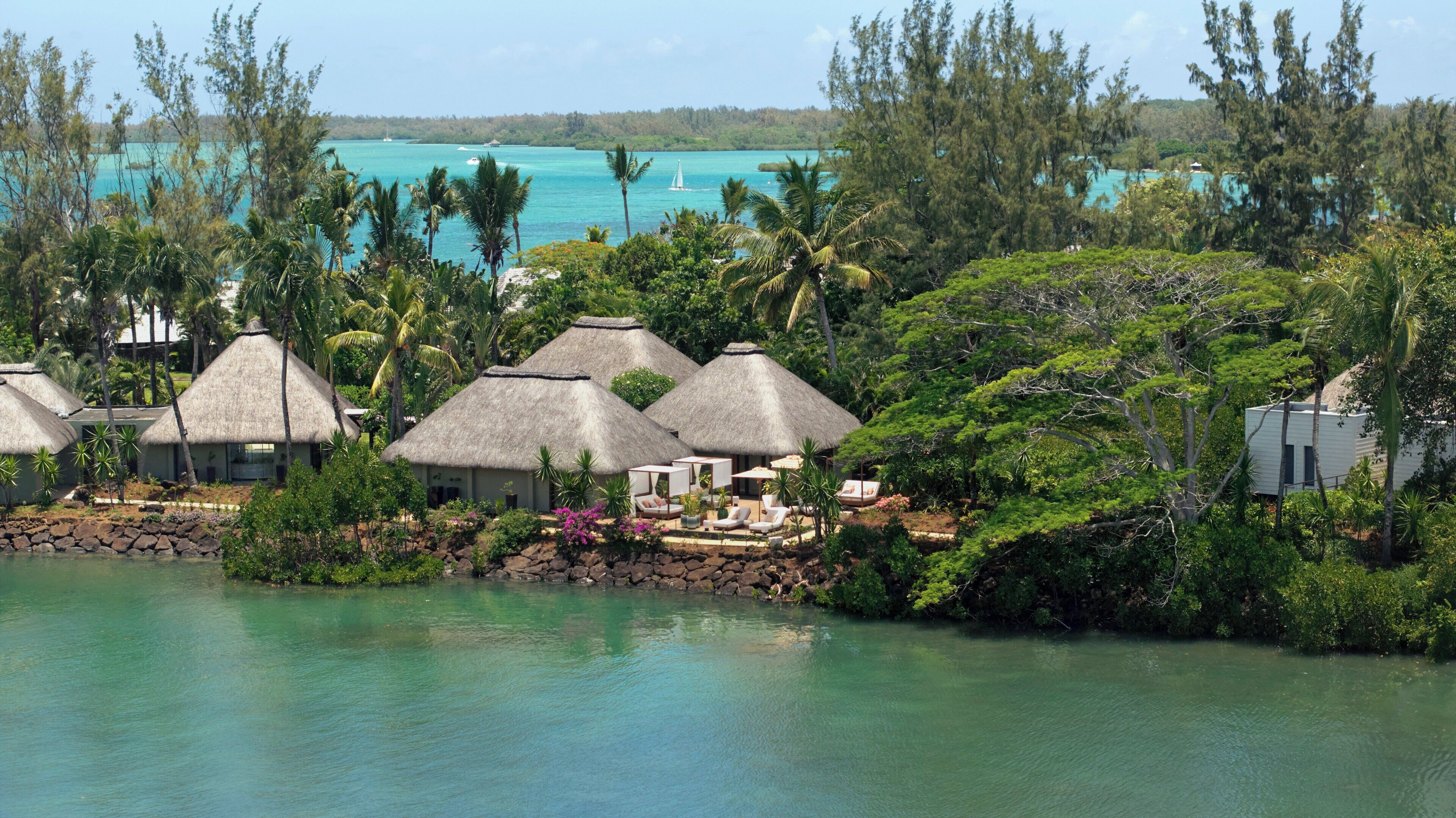 Un resort con cabañas de techo de paja, una piscina y abundante vegetación.