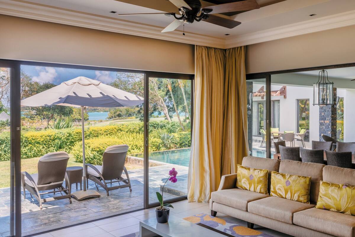 A spacious living room with a large window, a ceiling fan, and a sofa with decorative pillows.