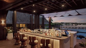 Zona de bar con mostrador, taburetes y vista a un cuerpo de agua al atardecer.