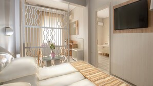 A hotel room with a sofa, a TV mounted on the wall, a potted plant, and a decorative partition. - Hotel Strass (Katerini)