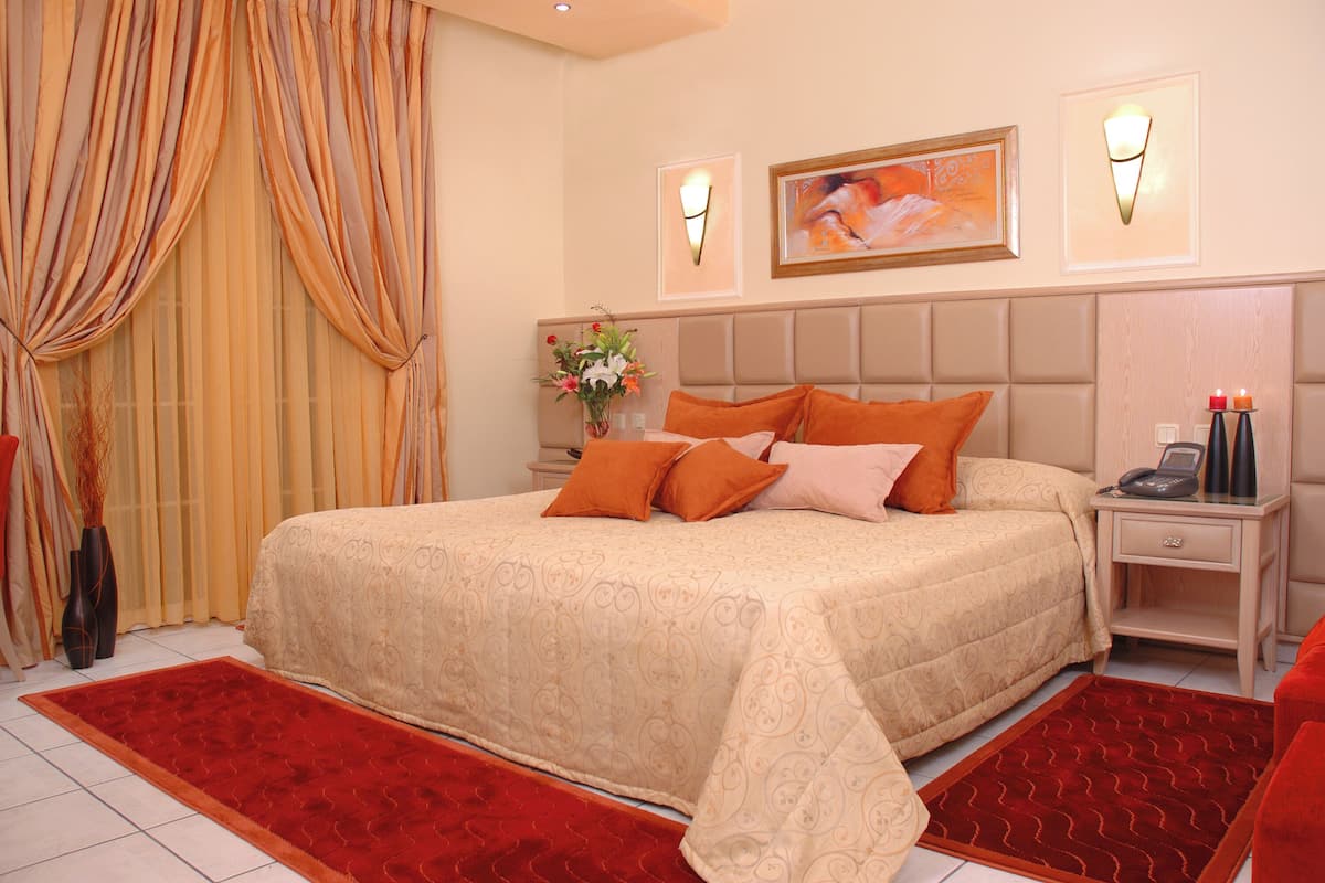 Una habitación de hotel con una cama grande, una mesita de noche con un teléfono y velas, un florero con flores y un cuadro en la pared.