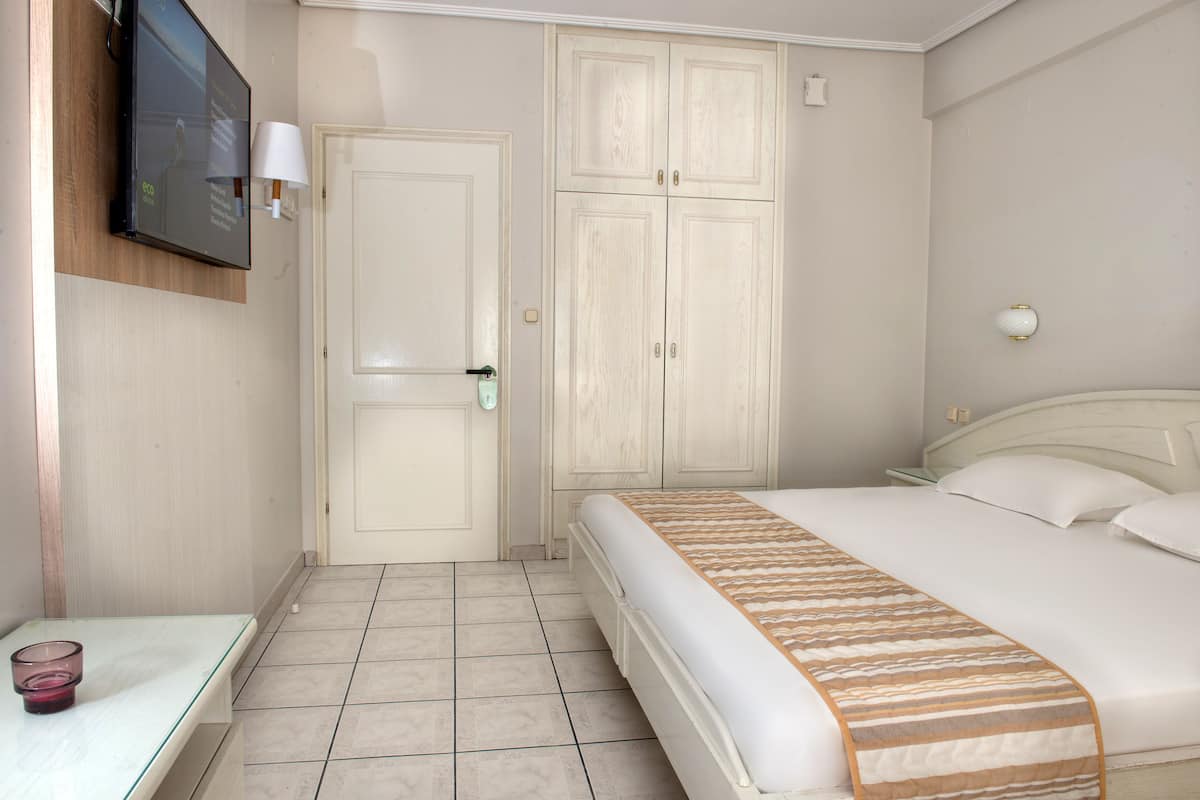 Habitación de hotel con cama, televisor montado en la pared, mesita de noche con lámpara y armario.