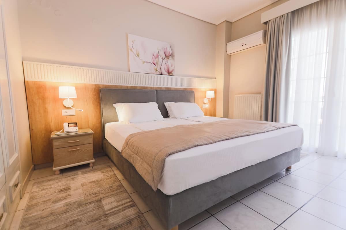 Un dormitorio ordenado con una cama grande, lámparas de noche, una mesita de noche y un aire acondicionado instalado en la pared.