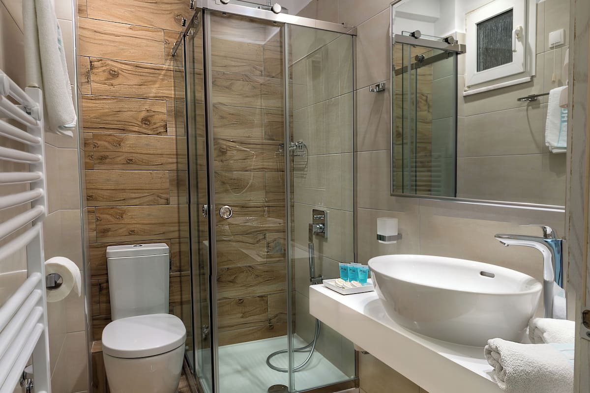 Un baño moderno con cabina de ducha de vidrio, inodoro, lavamanos con espejo y suelo de madera.