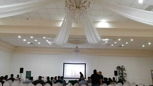 A conference room with white chairs, a projector screen, and a chandelier. - Hotel El Cason and Suites (Chihuahua)